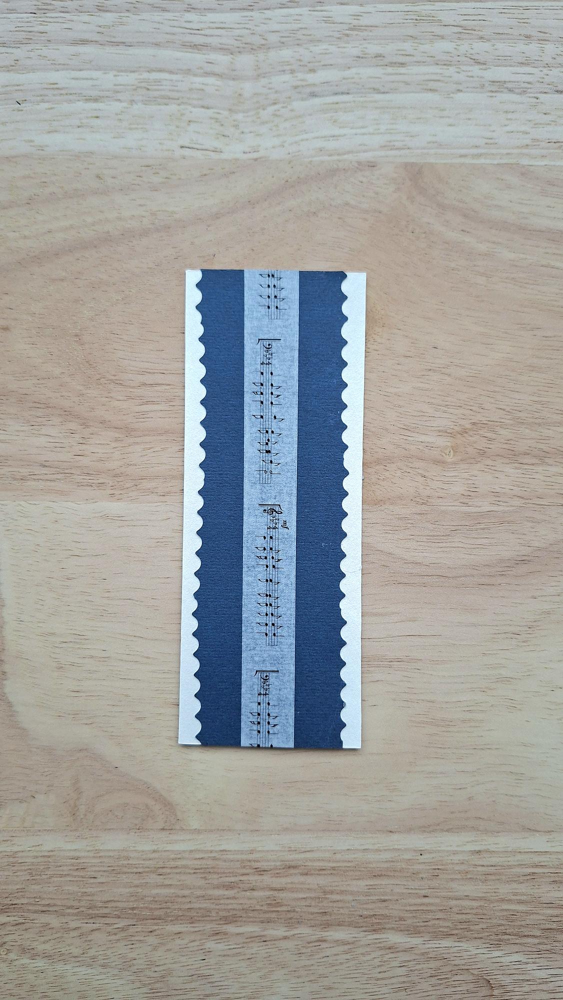 Back of music bookmark with sheet-music stripe, deep blue panels and pale scalloped edges.