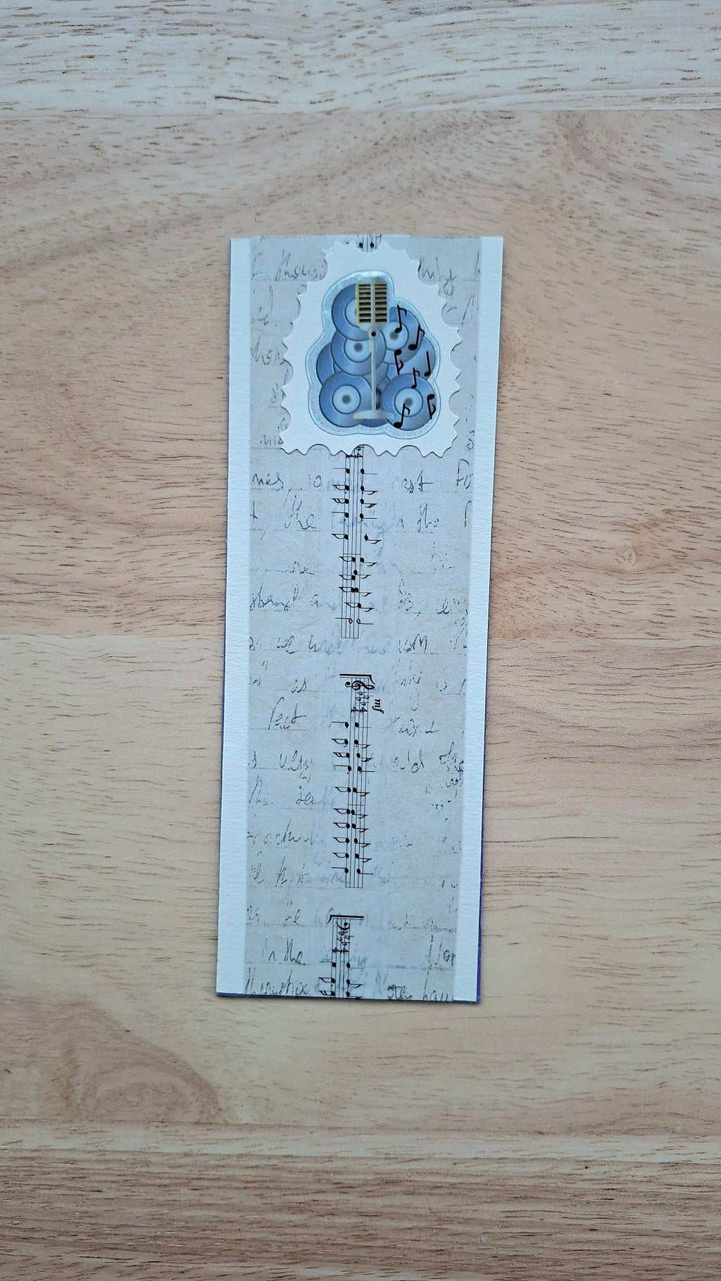 Music bookmark front with microphone, speakers, musical notes and beige handwriting-style pattern.