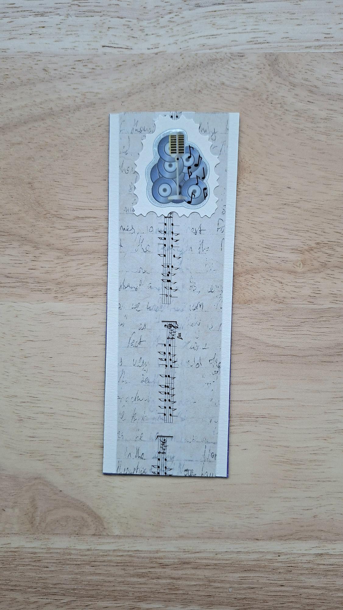 Music bookmark front with microphone, speakers, musical notes and beige handwriting-style pattern.